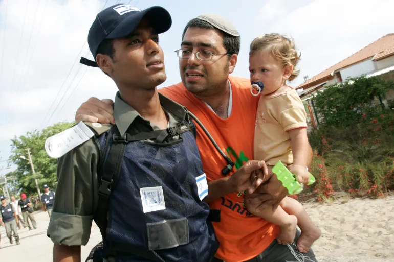 2005-08-17T000000Z_1638550411_RP6DRMSDZCAA_RTRMADP_3_MIDEAST-1747469713 Egy gyermekét cipelő telepes megpróbálja meggyőzni az izraeli rendőröket, hogy engedjék őket a Gázai övezet déli részén található Ganei Tal zsidó településen maradni 2005. augusztus 17-én.