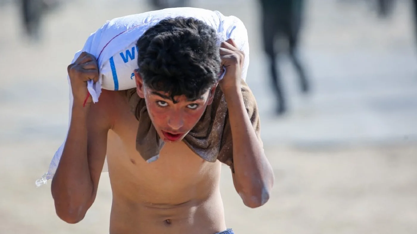 A displaced Palestinian youth ferries a bag of food aid on his shoulders after people stormed a World Food Programme warehouse in Deir el-Balah in the central Gaza Strip on May 28, 2025.jpg