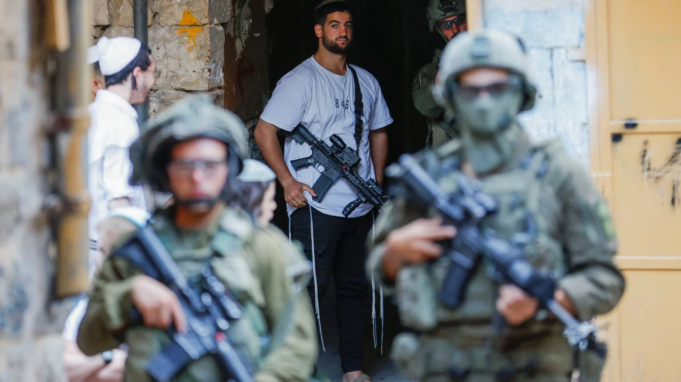 An armed settler stands near Israeli troops during a weekly settlers' tour in Hebron, in the Israeli-occupied West Bank, August 23, 2025. REUTERS_.jpg